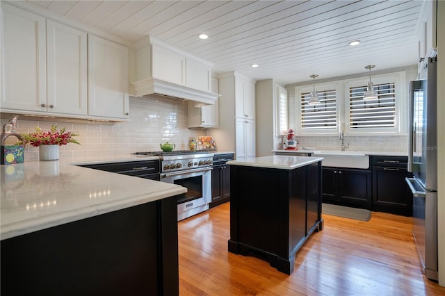 kitchen with sink, light wood-type flooring, high end appliances, a kitchen island, and pendant lighting