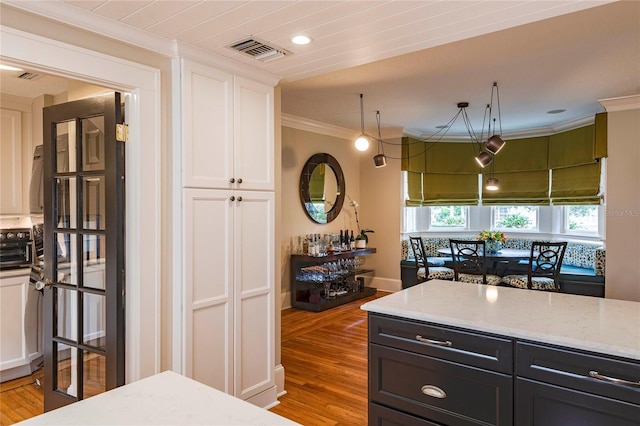 kitchen with white cabinets, light hardwood / wood-style floors, crown molding, and light stone countertops