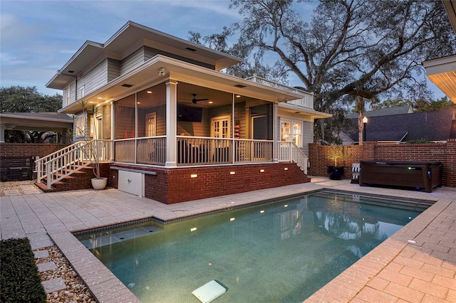 pool at dusk featuring a sunroom, a patio, ceiling fan, and a hot tub