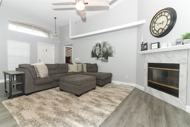 living room with ceiling fan, wood-type flooring, a premium fireplace, and a towering ceiling