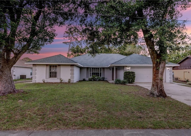 ranch-style house with a garage, central AC, concrete driveway, a lawn, and stucco siding