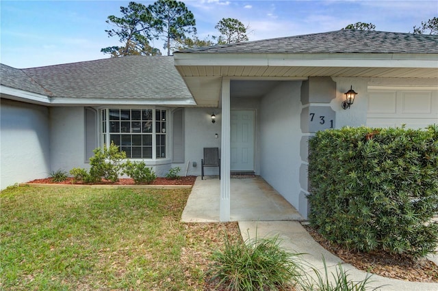 doorway to property featuring an attached garage, a shingled roof, a lawn, and stucco siding