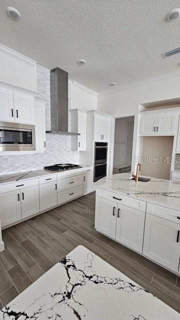 kitchen featuring wall chimney exhaust hood, stainless steel appliances, tasteful backsplash, crown molding, and white cabinets