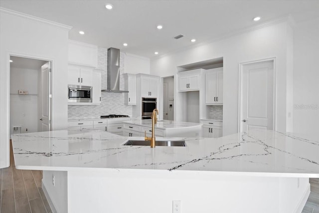 kitchen featuring wall chimney exhaust hood, sink, white cabinetry, a large island with sink, and stainless steel appliances