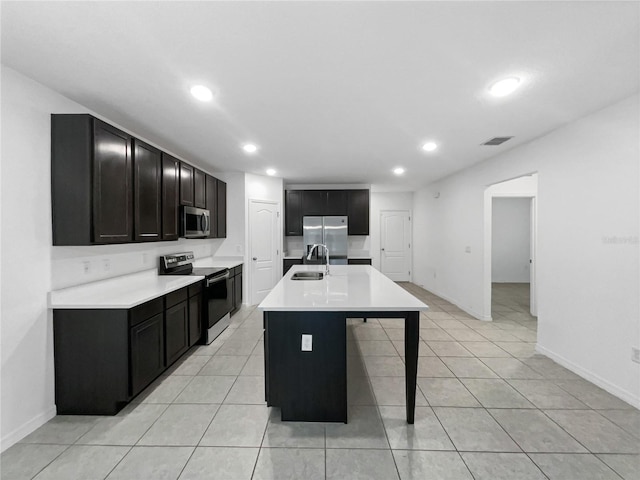 kitchen featuring sink, a kitchen bar, a kitchen island with sink, light tile patterned floors, and appliances with stainless steel finishes