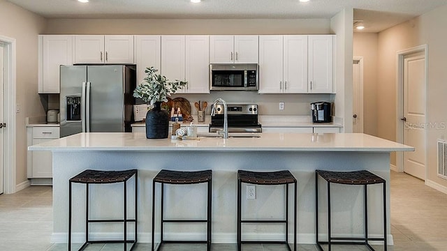 kitchen featuring white cabinets, a breakfast bar, stainless steel appliances, and a kitchen island with sink