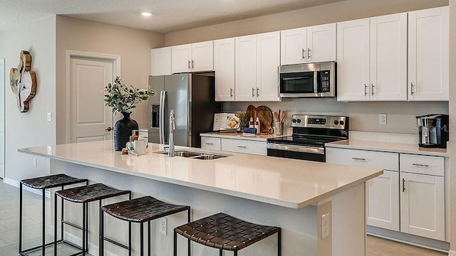 kitchen featuring a breakfast bar, white cabinetry, stainless steel appliances, and a kitchen island with sink