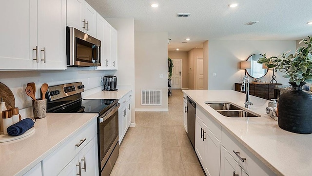 kitchen featuring appliances with stainless steel finishes, a textured ceiling, white cabinetry, and sink