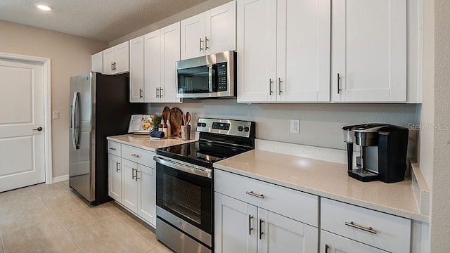 kitchen featuring light tile patterned floors, a textured ceiling, stainless steel appliances, and white cabinetry