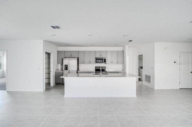 kitchen with sink, gray cabinets, stainless steel appliances, and an island with sink