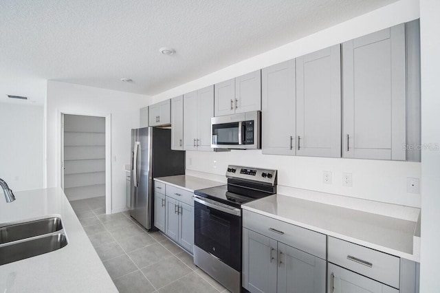 kitchen with sink, a textured ceiling, light tile patterned floors, gray cabinets, and stainless steel appliances