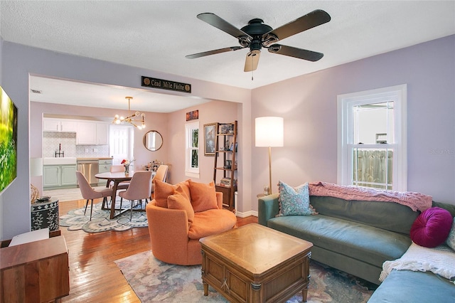 living room with a textured ceiling, a wealth of natural light, ceiling fan with notable chandelier, and light wood-type flooring