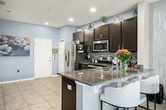 kitchen with dark stone countertops, tasteful backsplash, dark brown cabinets, kitchen peninsula, and stainless steel appliances