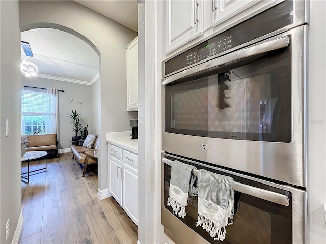 kitchen with light hardwood / wood-style flooring, white cabinets, stainless steel double oven, and ornamental molding