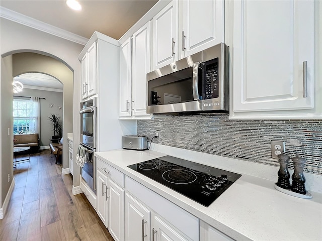 kitchen with white cabinetry, backsplash, light wood-type flooring, appliances with stainless steel finishes, and ornamental molding