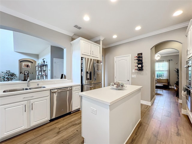 kitchen with appliances with stainless steel finishes, a kitchen island, sink, light hardwood / wood-style floors, and white cabinetry