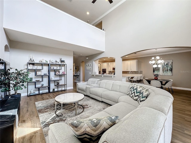 living room featuring hardwood / wood-style floors, a high ceiling, ceiling fan with notable chandelier, and ornamental molding