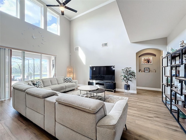 living room with ceiling fan, wood-type flooring, a towering ceiling, and a wealth of natural light