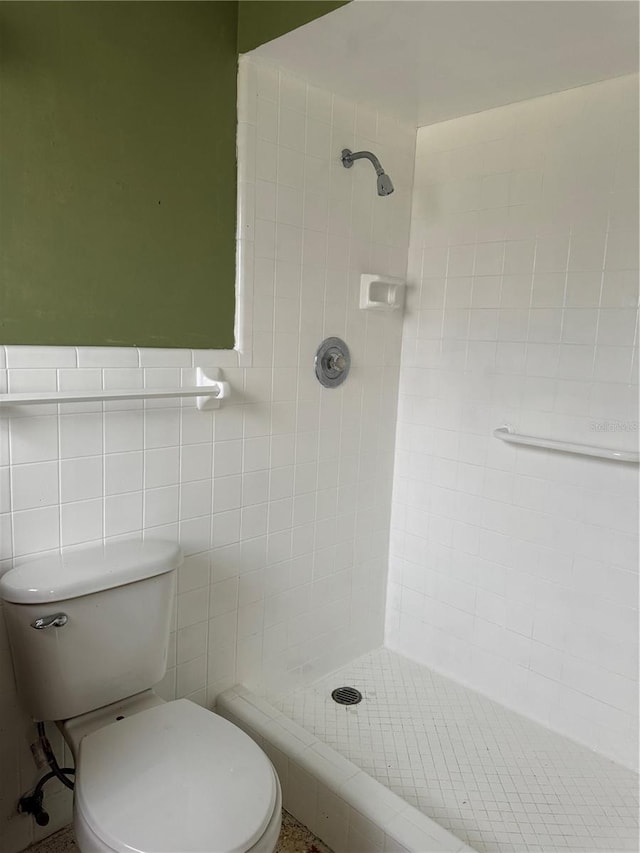 bathroom with a tile shower, toilet, and tile walls