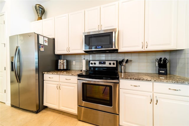 kitchen with stone counters, white cabinetry, stainless steel appliances, and light tile patterned floors