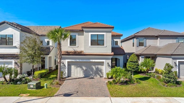 view of front facade with decorative driveway, a tile roof, stucco siding, an attached garage, and a front lawn