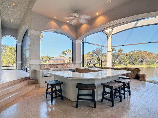 view of patio featuring exterior bar, a water view, and ceiling fan