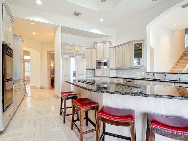 kitchen with built in appliances, dark stone countertops, kitchen peninsula, a breakfast bar area, and decorative backsplash