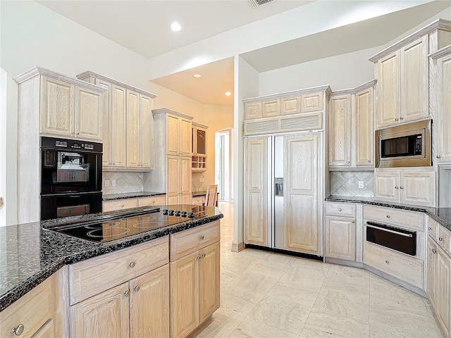 kitchen featuring light brown cabinetry, backsplash, dark stone counters, and black appliances