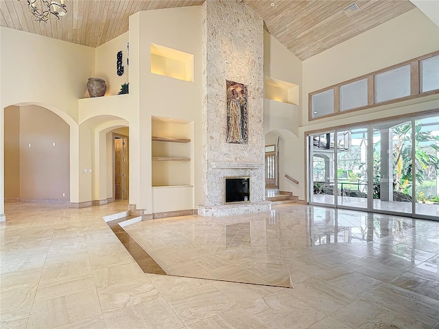 unfurnished living room with built in shelves, a stone fireplace, wooden ceiling, and a high ceiling