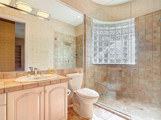 bathroom featuring a tile shower, vanity, tile walls, tile patterned flooring, and toilet