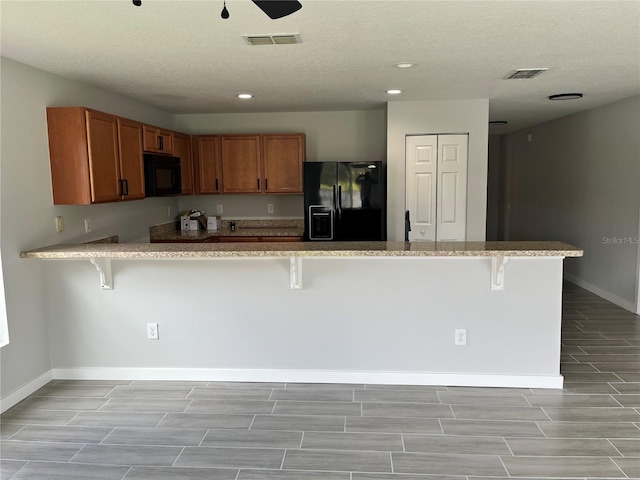 kitchen featuring kitchen peninsula, ceiling fan, a breakfast bar area, and black appliances