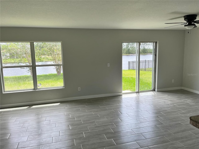 empty room featuring ceiling fan, plenty of natural light, and a water view