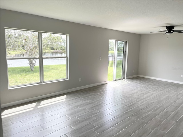 unfurnished room with ceiling fan and a water view