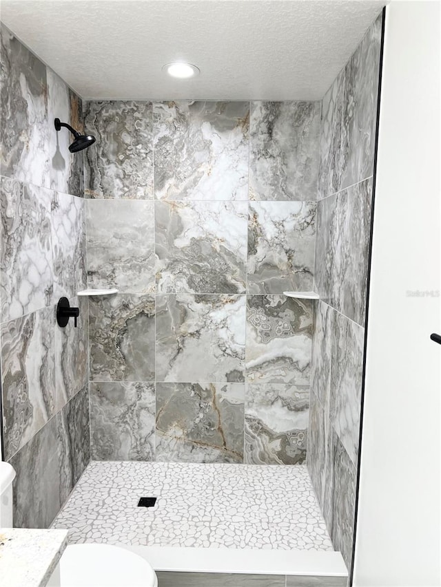 bathroom with a tile shower, a textured ceiling, and toilet