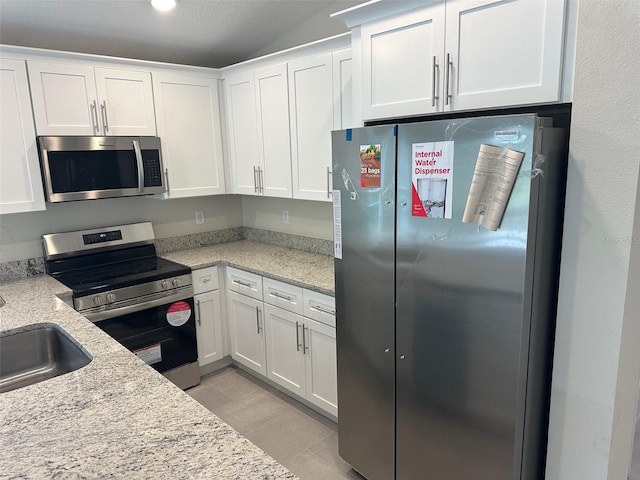 kitchen featuring white cabinetry, appliances with stainless steel finishes, lofted ceiling, light stone countertops, and sink