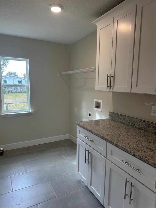 washroom featuring hookup for an electric dryer, light tile patterned flooring, hookup for a washing machine, a textured ceiling, and cabinets