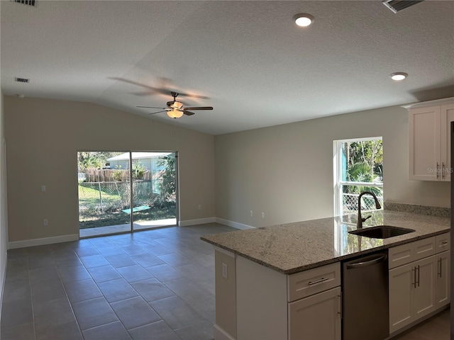 kitchen with light stone countertops, stainless steel dishwasher, vaulted ceiling, sink, and white cabinetry