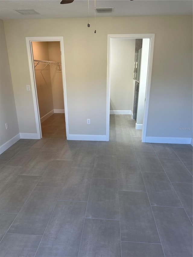 unfurnished bedroom with a spacious closet, dark tile patterned floors, ceiling fan, and a closet