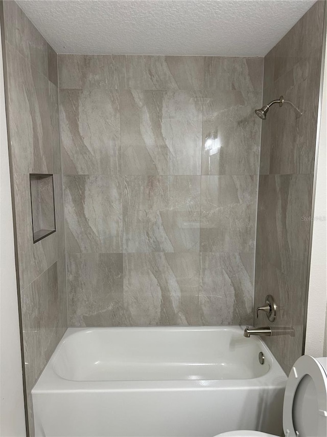 bathroom with a textured ceiling, toilet, and tiled shower / bath