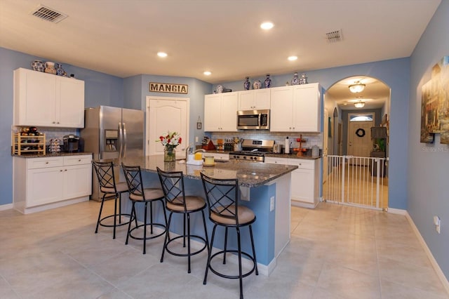 kitchen featuring dark stone counters, a center island with sink, appliances with stainless steel finishes, white cabinetry, and a breakfast bar area