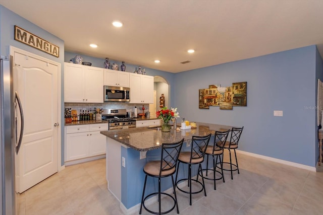 kitchen featuring white cabinetry, an island with sink, dark stone counters, a breakfast bar, and appliances with stainless steel finishes