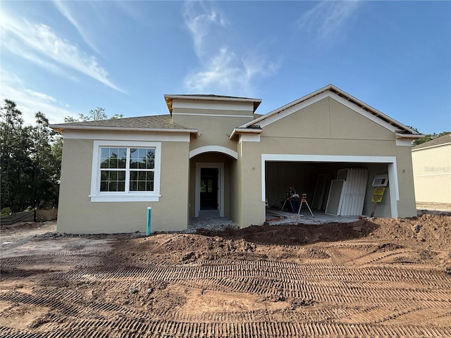 view of front facade with an attached garage, dirt driveway, and stucco siding