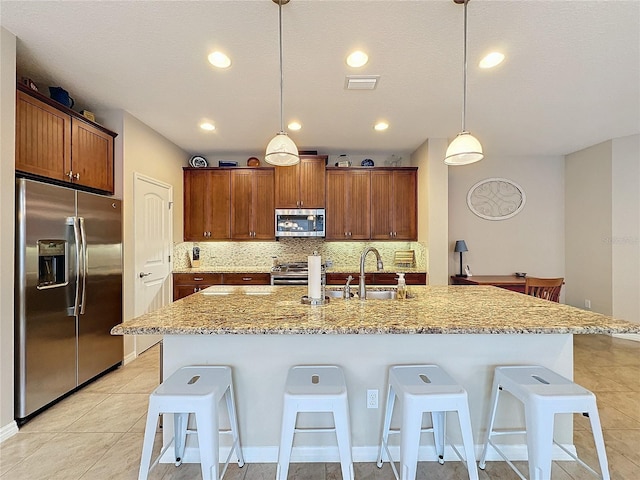 kitchen with hanging light fixtures, stainless steel appliances, backsplash, an island with sink, and a breakfast bar area