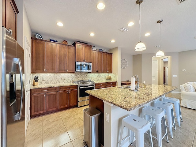 kitchen featuring a kitchen breakfast bar, stainless steel appliances, a kitchen island with sink, sink, and hanging light fixtures