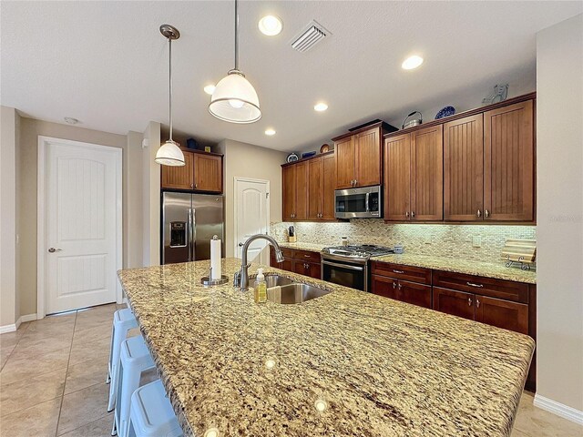 kitchen with a kitchen breakfast bar, stainless steel appliances, sink, light tile patterned floors, and a center island with sink