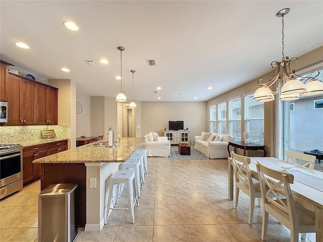 kitchen with light stone countertops, stainless steel appliances, sink, decorative light fixtures, and a breakfast bar area