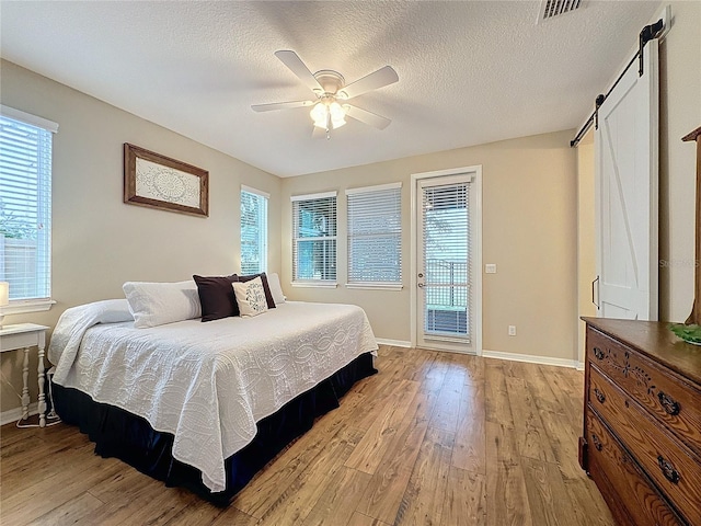 bedroom featuring access to outside, ceiling fan, a barn door, light wood-type flooring, and a textured ceiling