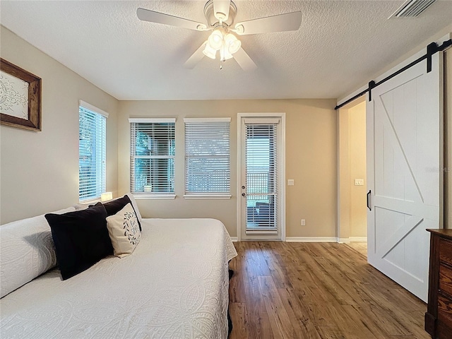 bedroom with access to exterior, ceiling fan, a barn door, hardwood / wood-style floors, and multiple windows