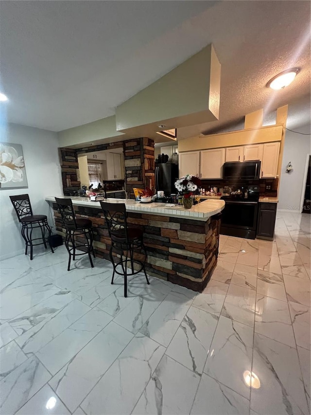 kitchen featuring backsplash, black appliances, white cabinets, a textured ceiling, and tile counters