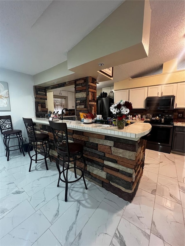 kitchen with kitchen peninsula, electric stove, tile counters, and white cabinets